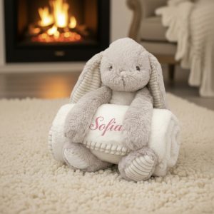 Soft plush bunny toy holding a personalised blanket with the name "Sofia" in a cozy living room sett.